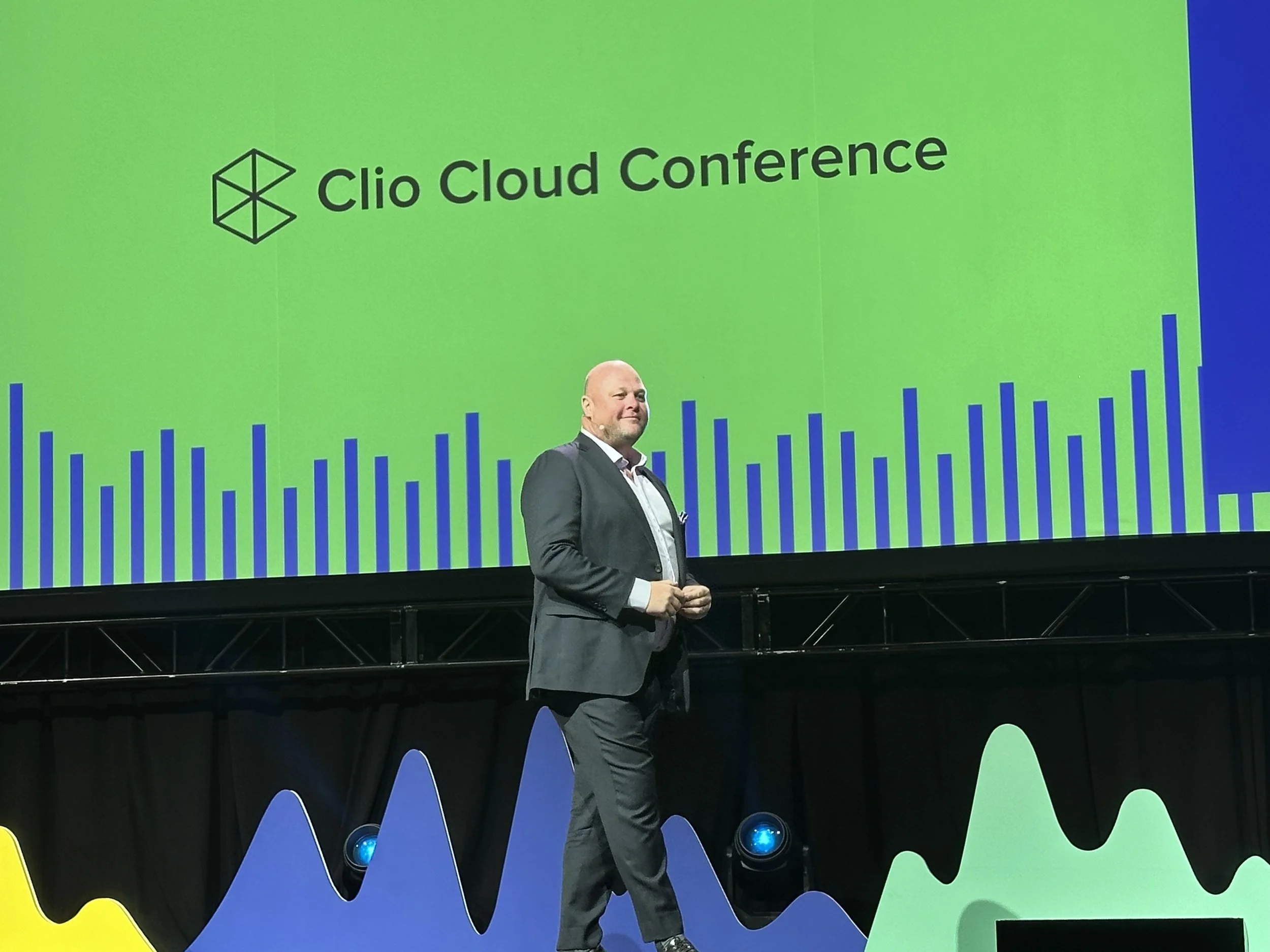 Jack Newton speaking onstage at the 2023 Clio Cloud Conference, with a green conference screen behind him