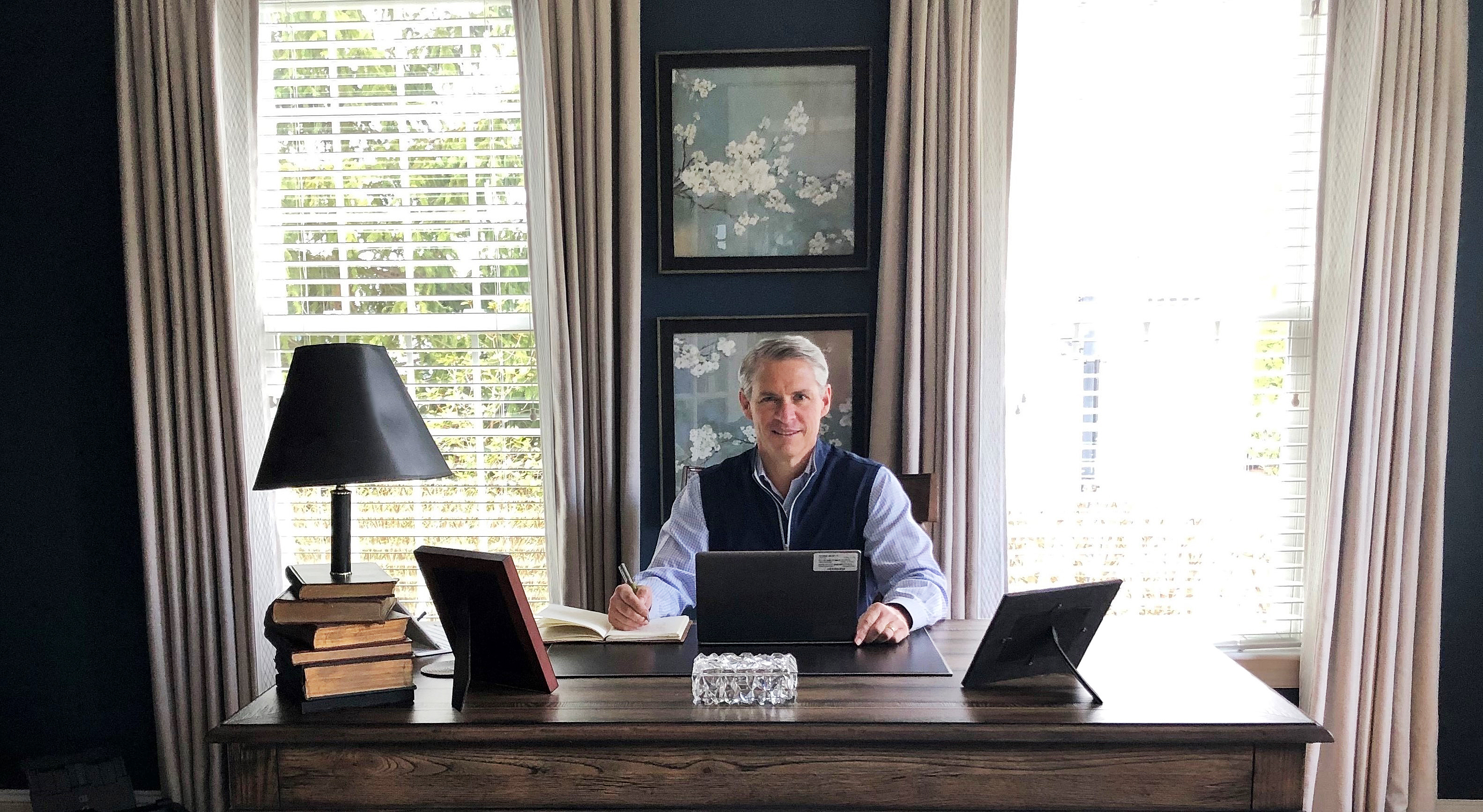 Jack Roche seated at a wooden desk in his home office, with a laptop, notebook, and books