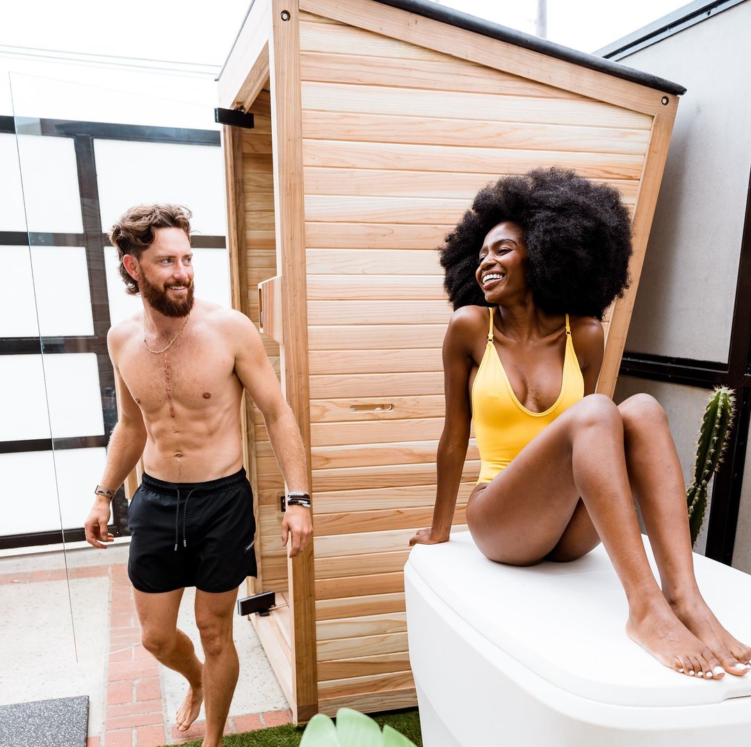 Two people beside a wooden sauna and a cold plunge tub