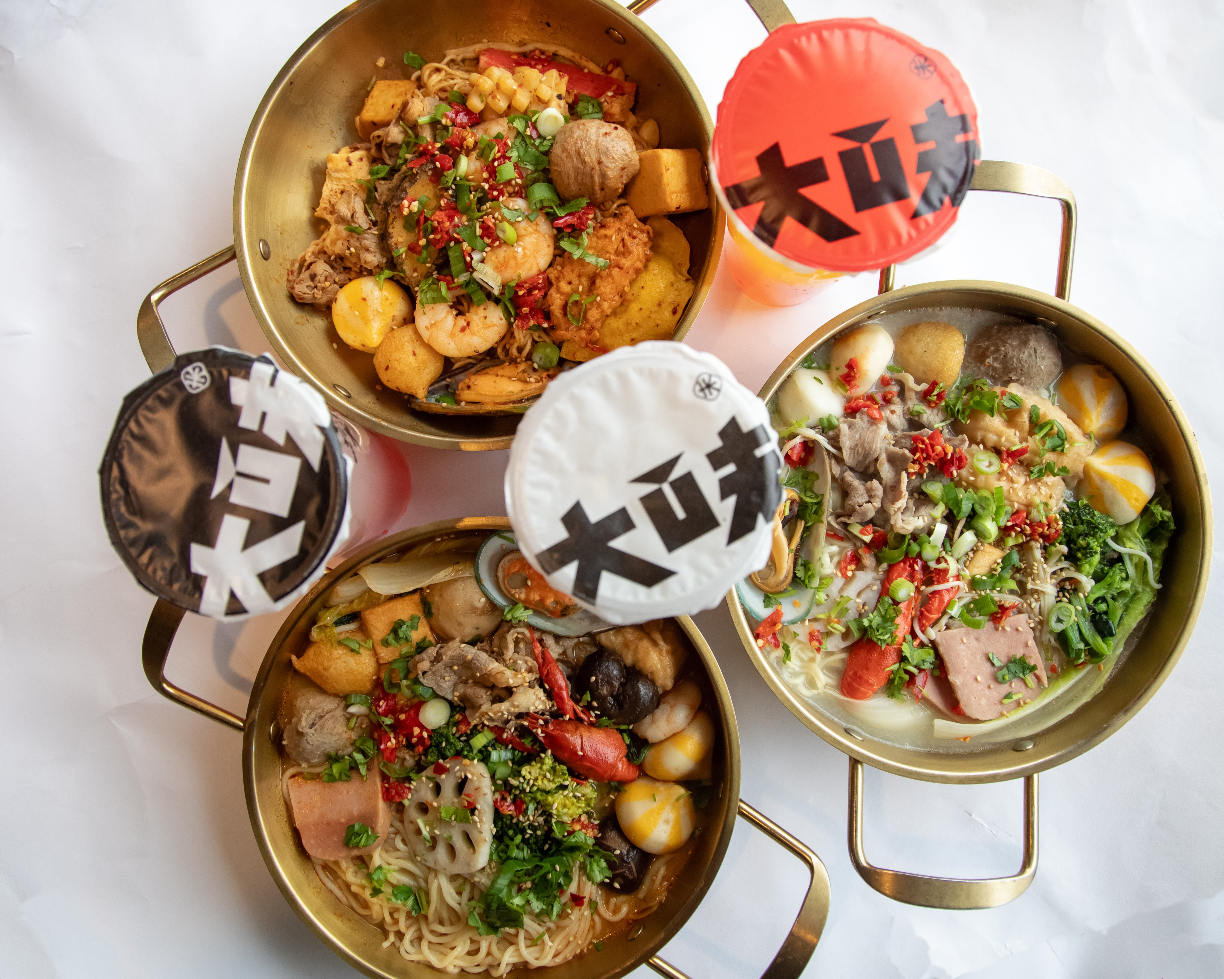 An individual golden hot pot filled with shrimp, mushrooms, vegetables and other ingredients in red broth