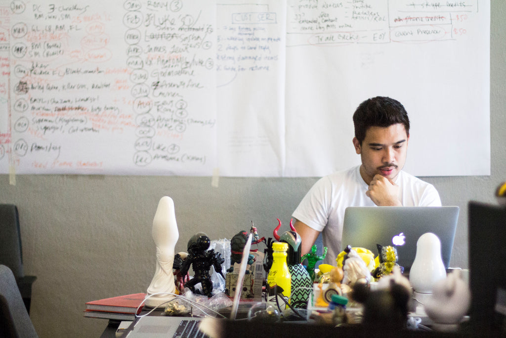Jackson Aw working at a laptop, surrounded by collectible figures, with planning sheets on the wall