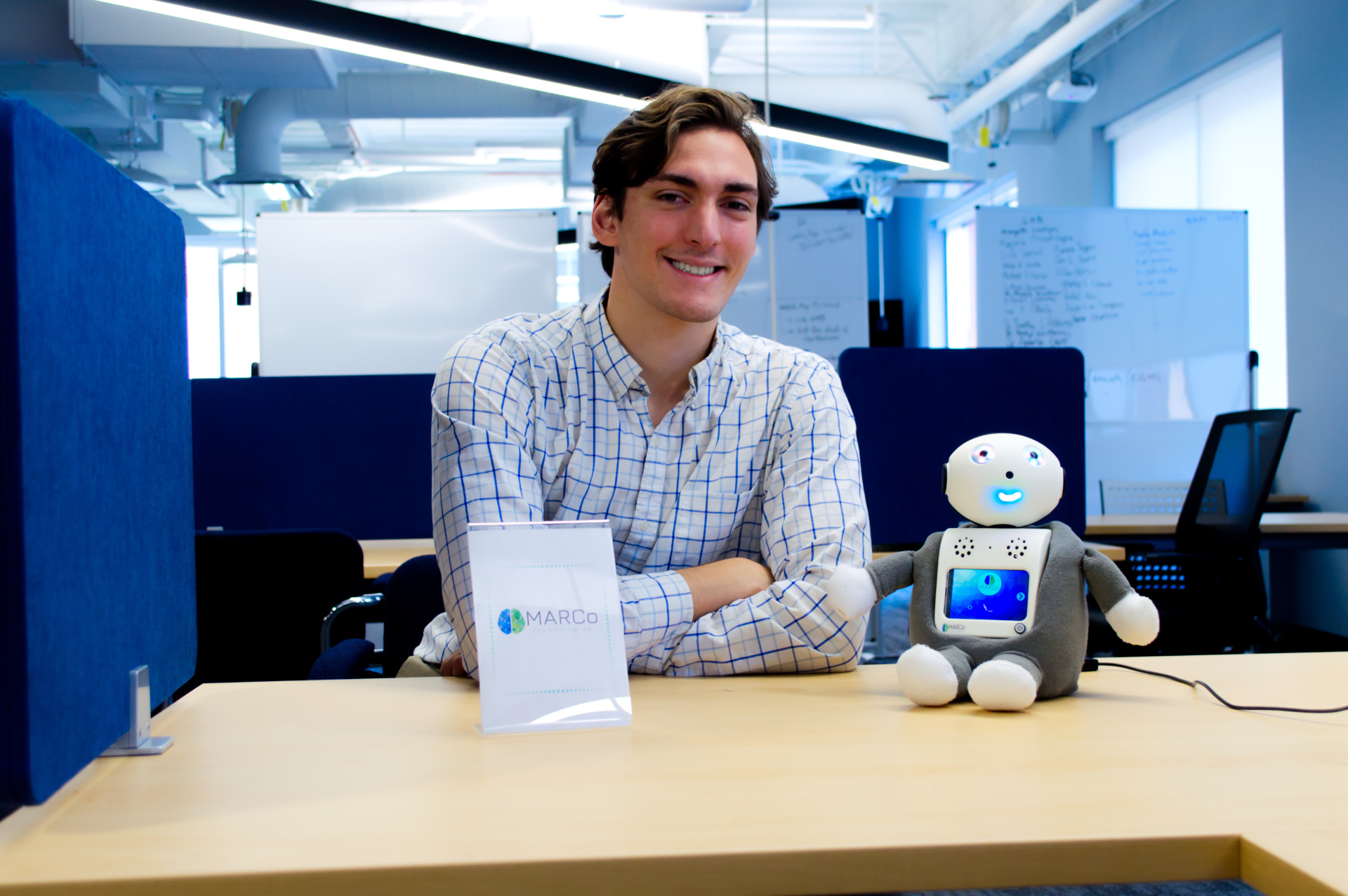 Jacob Boyle seated beside the MARCo conversational robot in a bright workspace