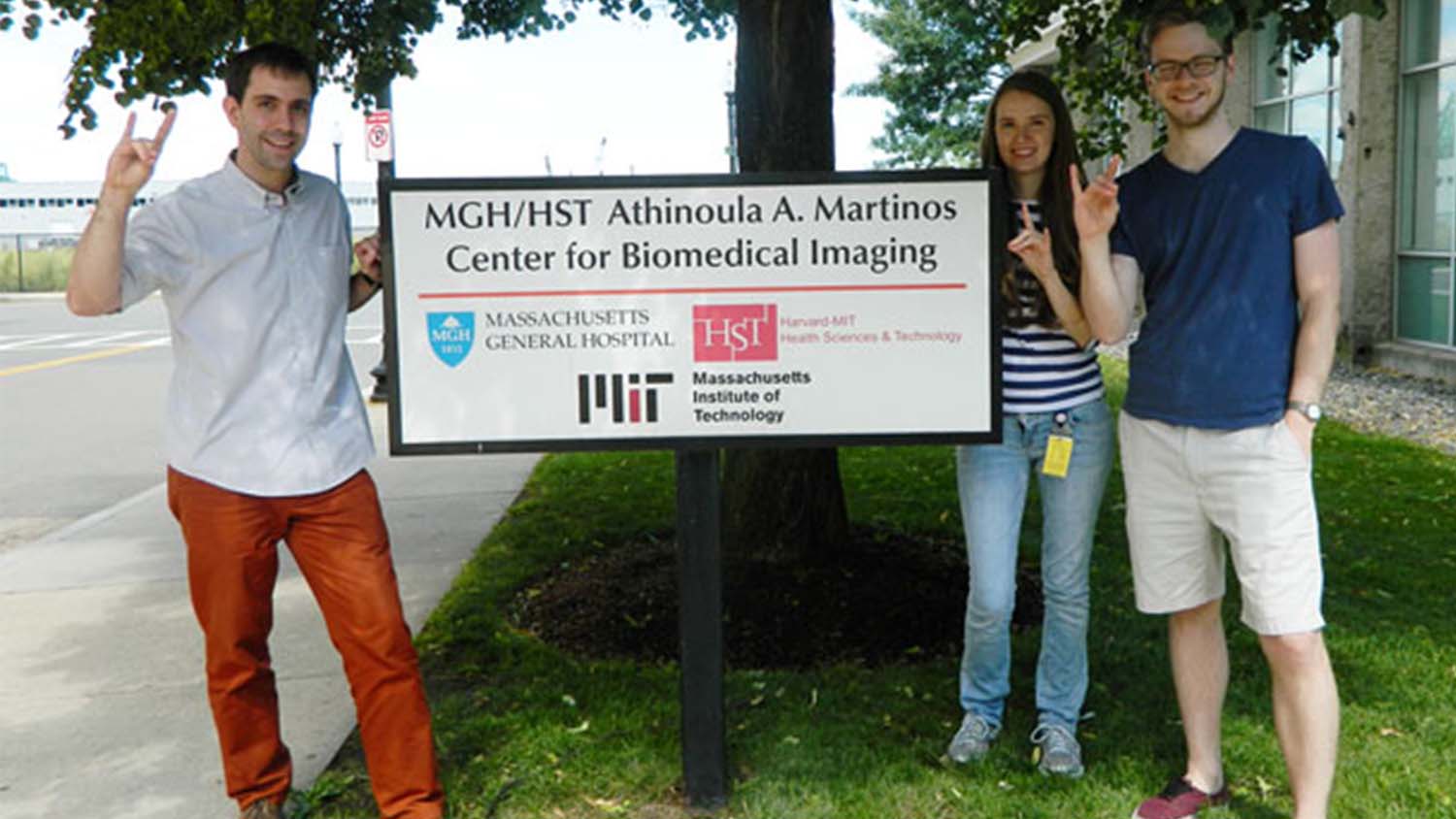 Jacob Hooker, Jaclyn Smith and Ian Hill making NC State hand gestures beside the Martinos Center sign