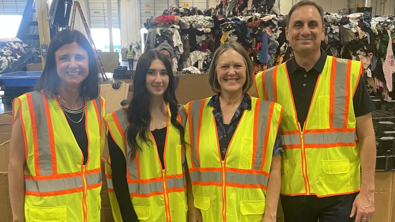 Jacob Slayton and three textile policy visitors wearing safety vests inside a clothing recovery facility