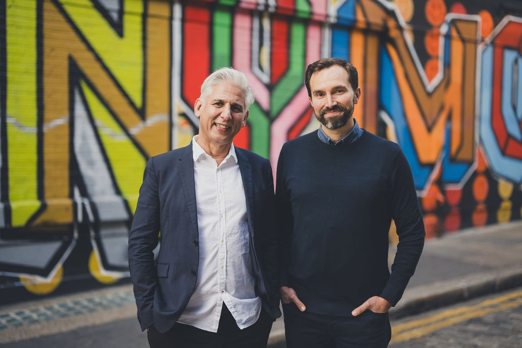 Robin Tuluie, left, and Jacomo Corbo standing together in front of a colorful mural