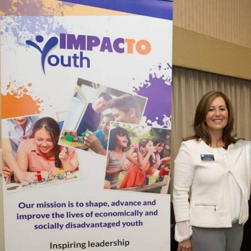Jackie Krick standing beside an IMPACTO Youth banner