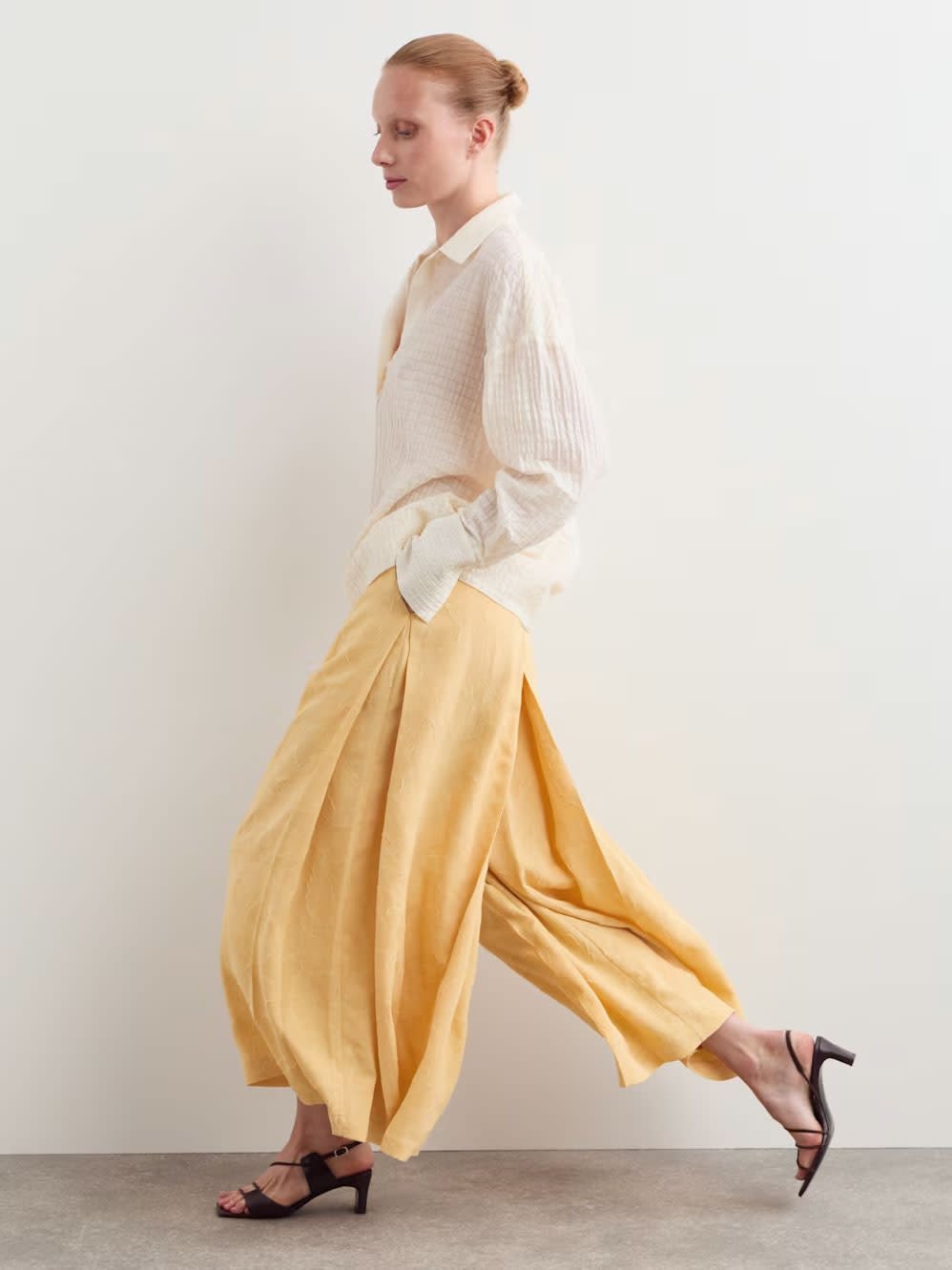 Jaeger summer 2026 look: a model wearing a pale shirt, flowing yellow trousers and dark sandals.