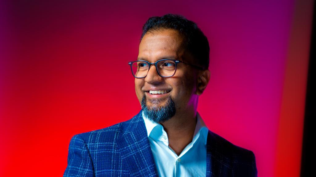 Jagath Wanninayake in glasses and a blue checked jacket against a red and purple background