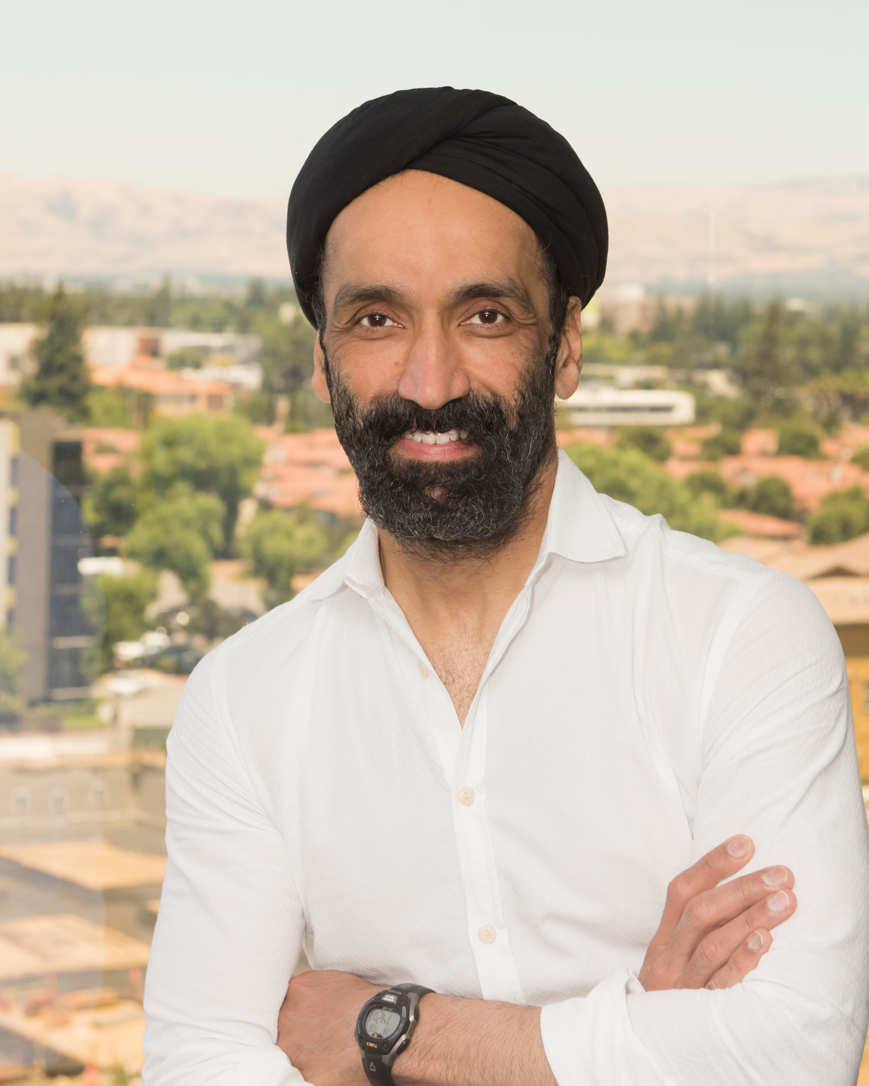 Jagdeep Singh standing before a window in a white shirt and black turban
