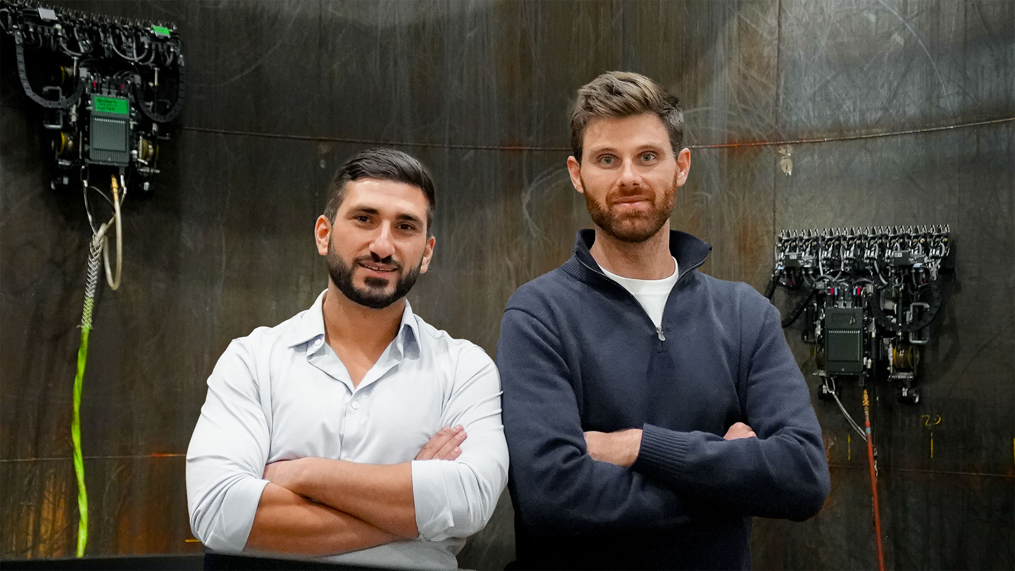 Jake Loosararian and Troy Demmer standing inside an industrial test space with Gecko Robotics wall-crawling robots behind them