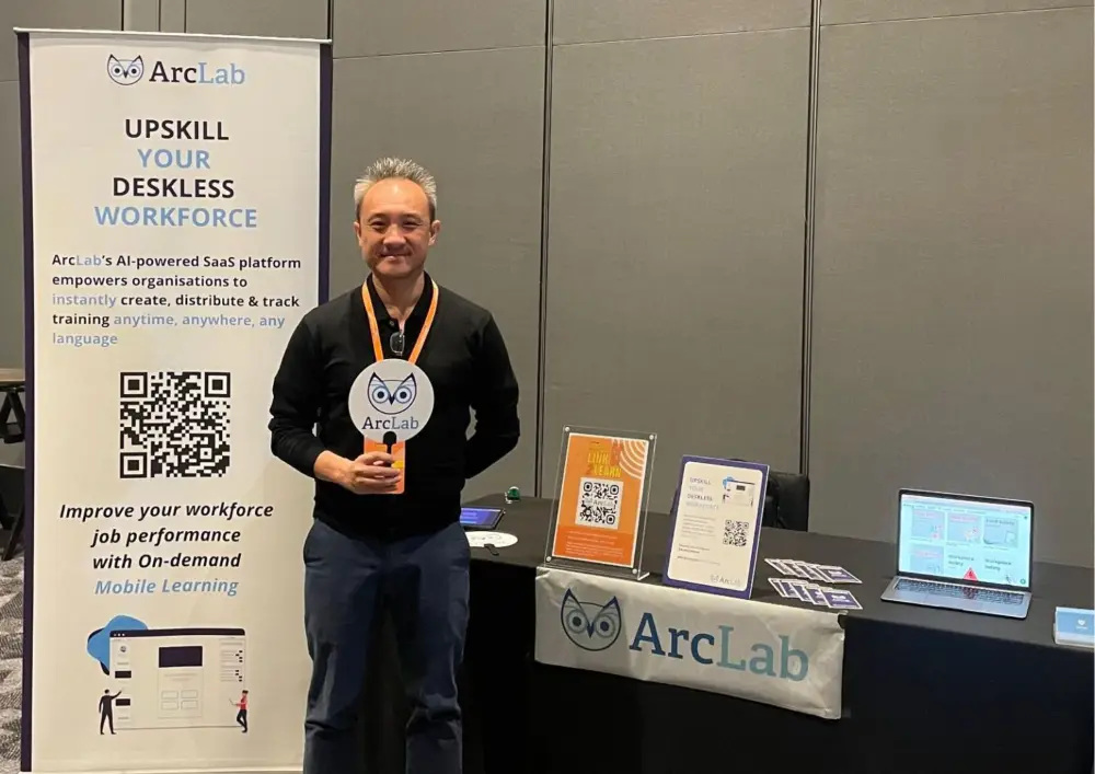 James Chia standing beside an ArcLab display and demonstration laptop at an exhibition booth
