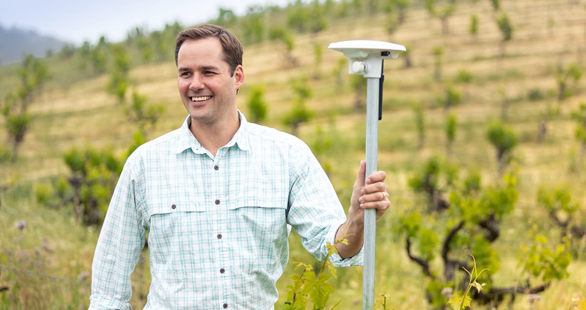 James Ethington standing in a vineyard beside an Arable field sensor