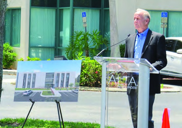 Jim Beré speaking at an outdoor lectern beside a rendering of Alta's planned Fort Myers office