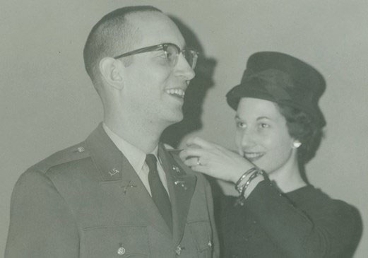 Young Jim Ferrell in Army uniform, smiling beside a woman adjusting his collar