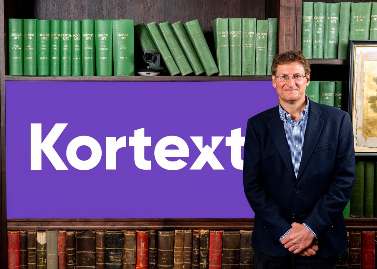 James Gray standing beside a purple Kortext sign in front of shelves of bound books