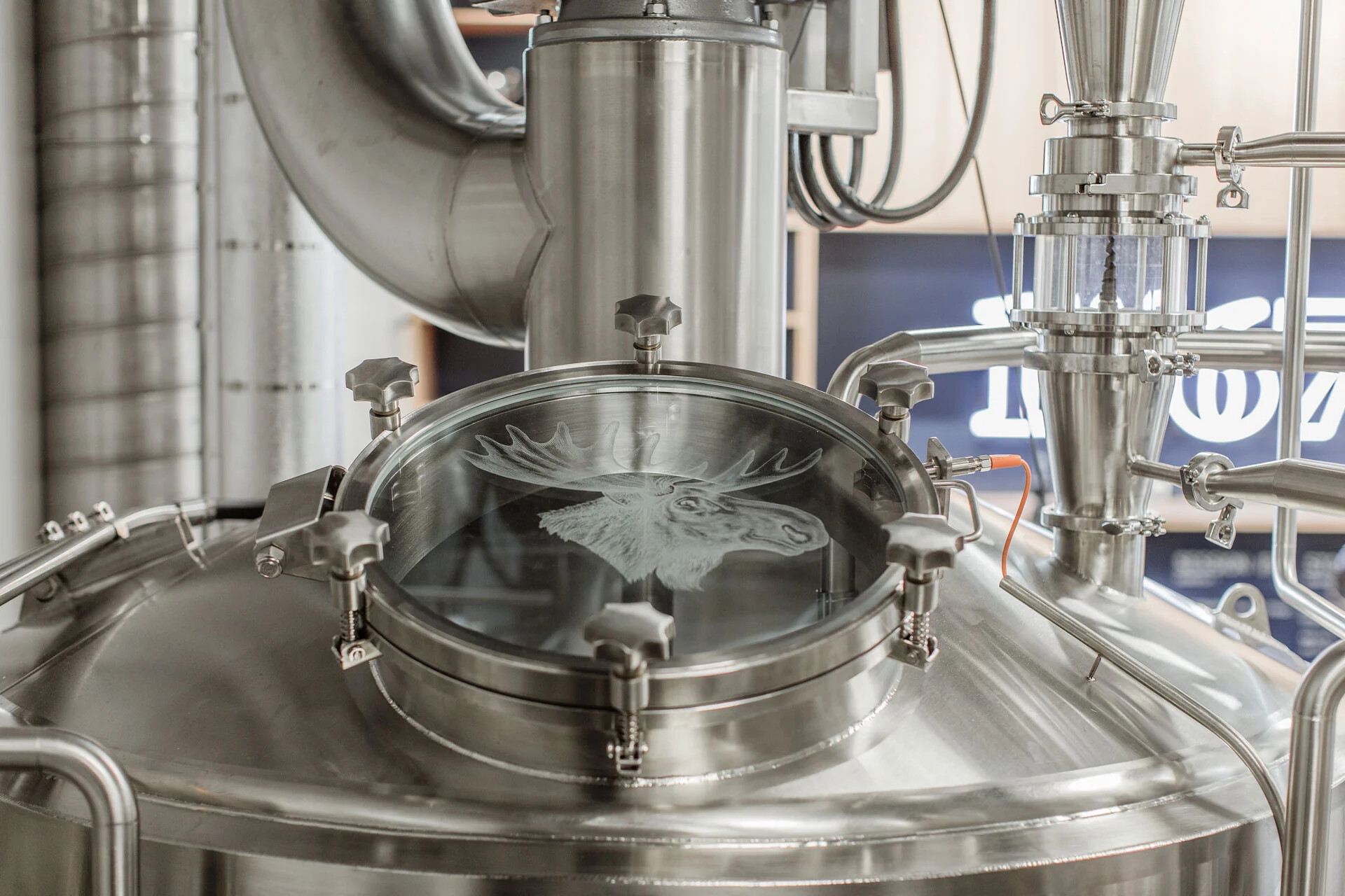 Polished brewing equipment with a moose etched into a circular glass hatch