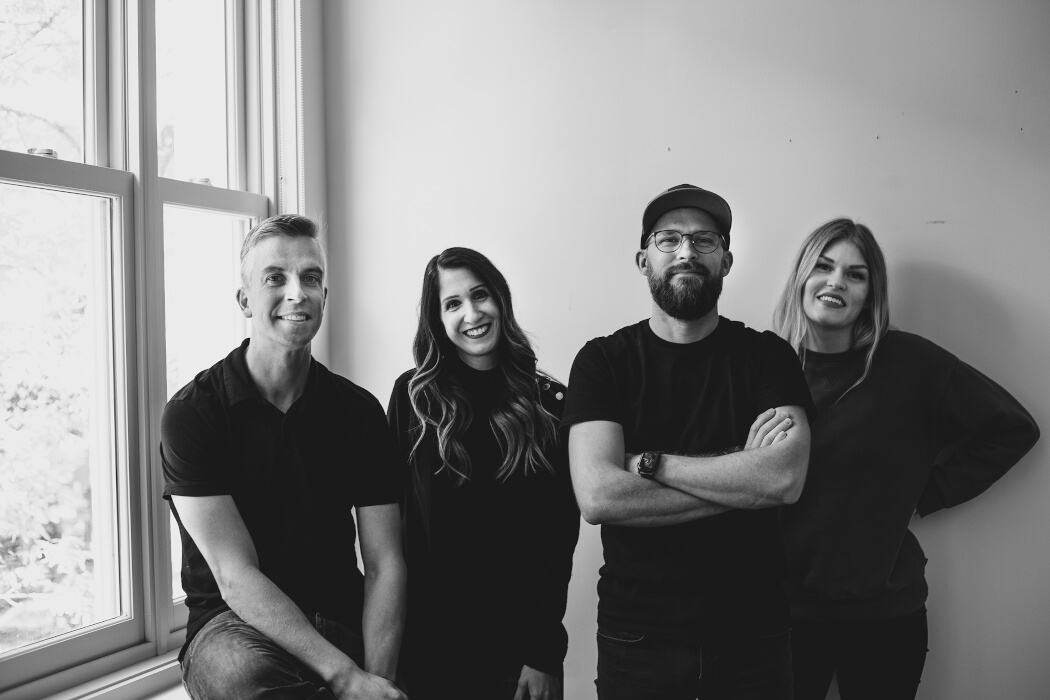 James Neufeld, second from right, with three samdesk colleagues beside an office window.