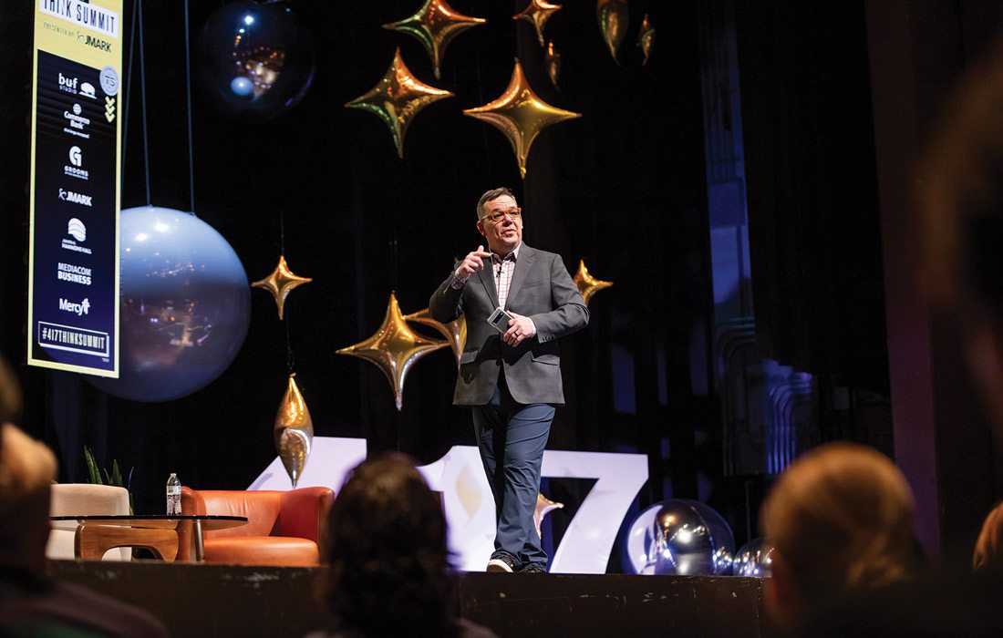 James Stapleton speaking on stage at Think Summit, surrounded by star-shaped balloons
