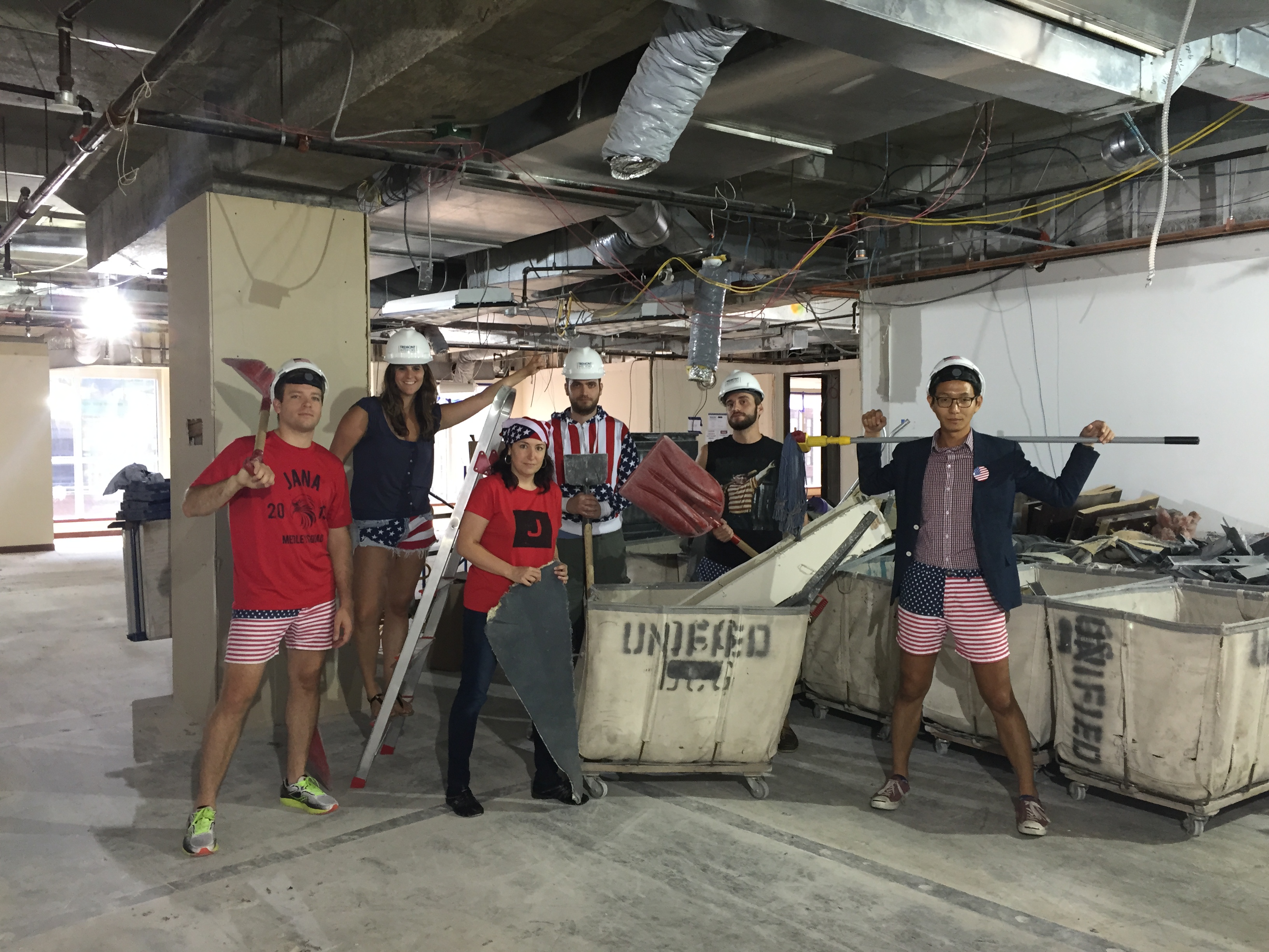 Jana employees wearing hard hats and holding tools in their unfinished Boston office