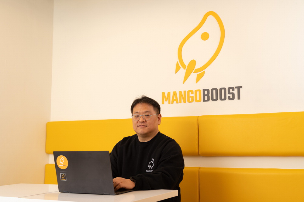 Jangwoo Kim working on a laptop in MangoBoost’s yellow office seating area