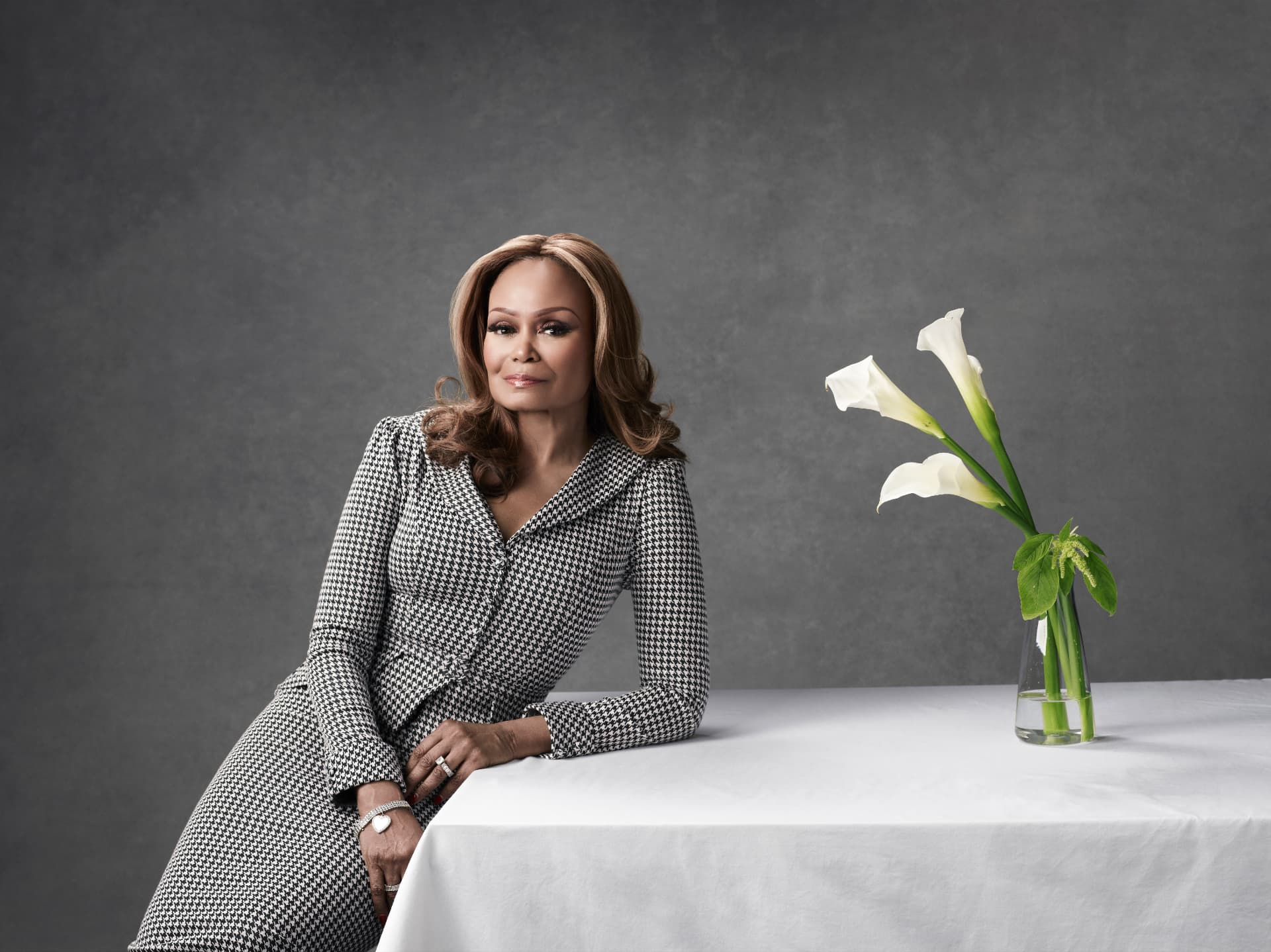 Janice Bryant Howroyd seated beside a table with white calla lilies, wearing a black and white patterned dress
