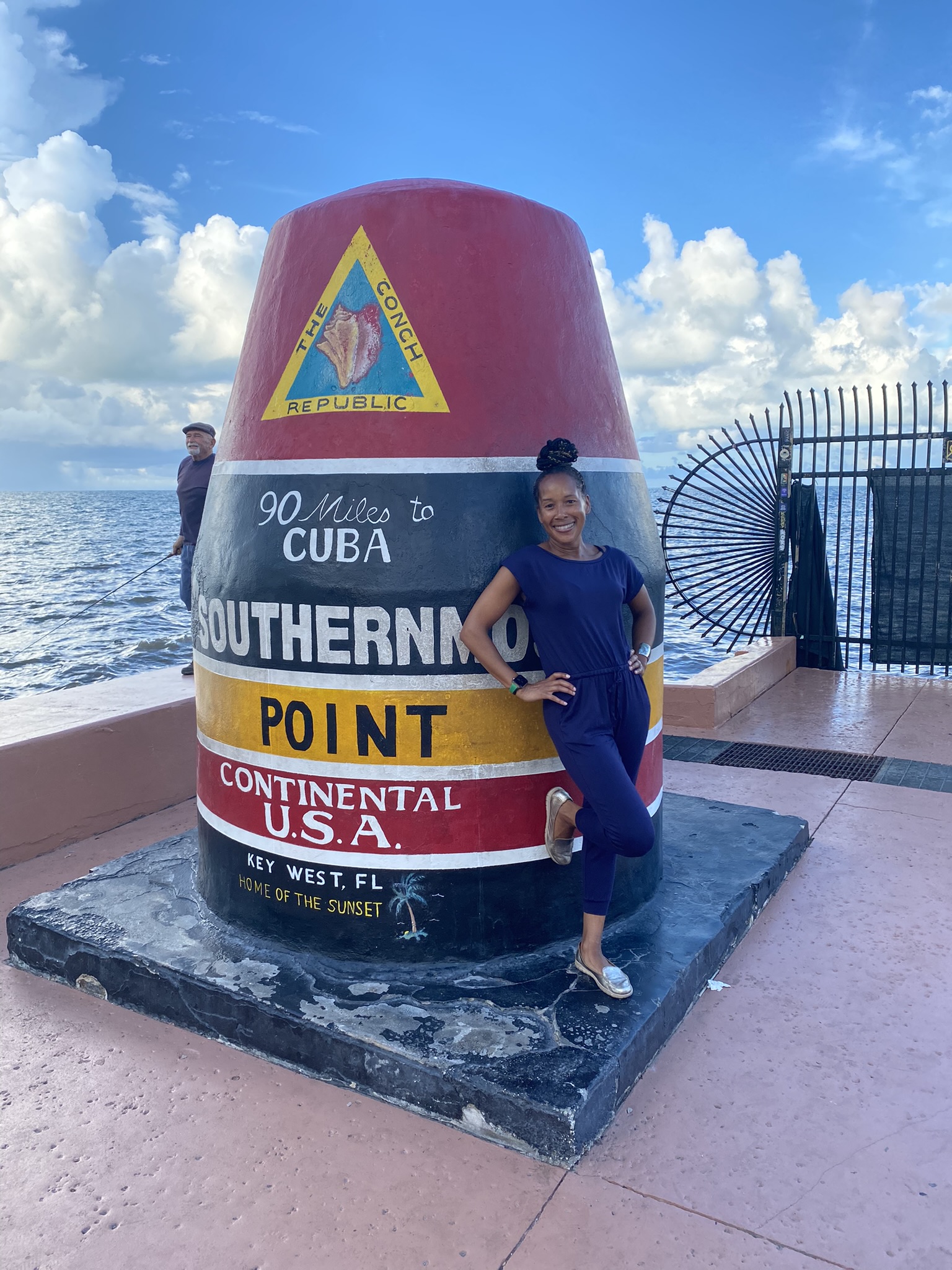 Janine Dawson standing beside the Southernmost Point marker in Key West, Florida