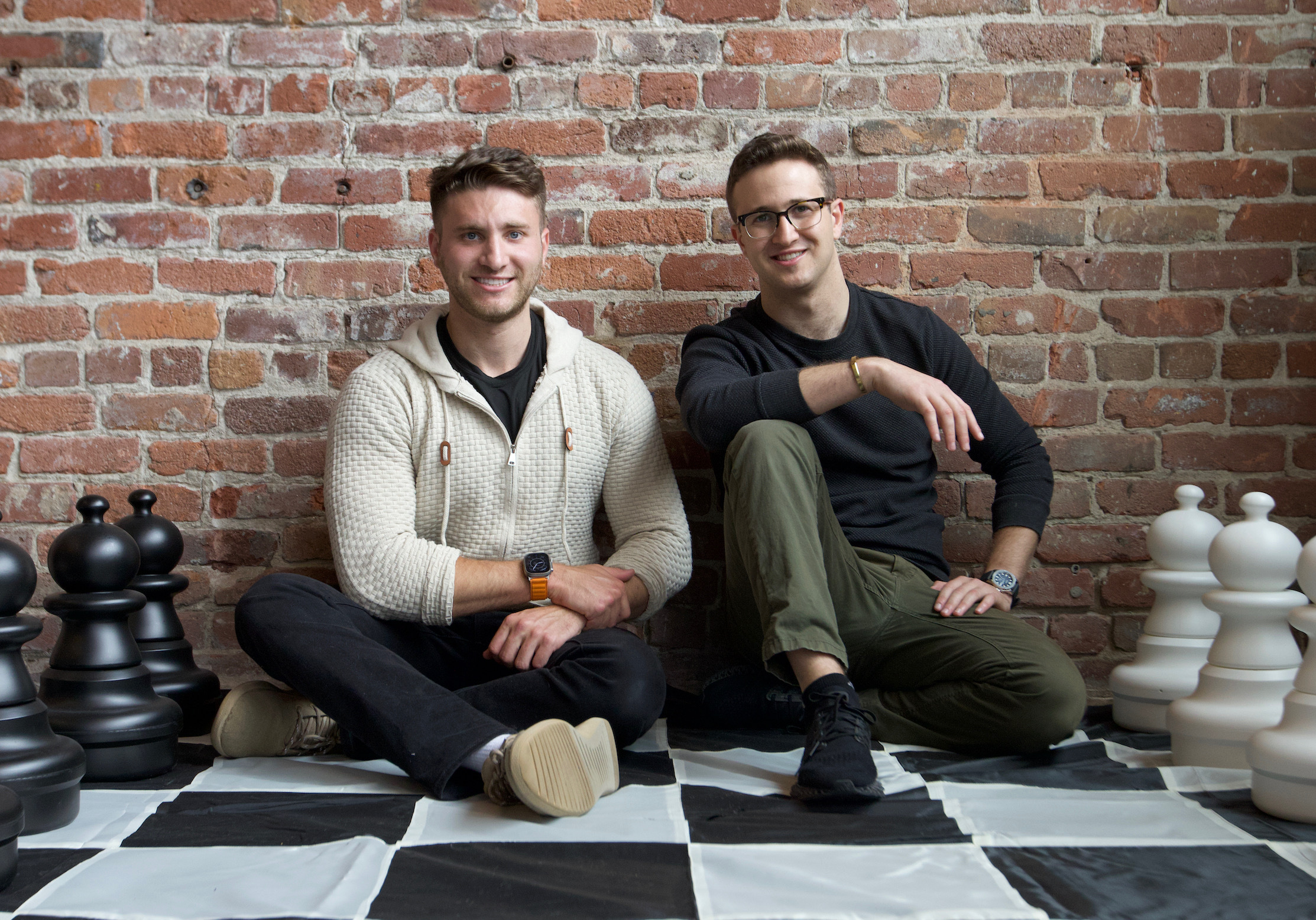 Jared Geller on the left and Jake Brooks on the right, seated among large chess pieces