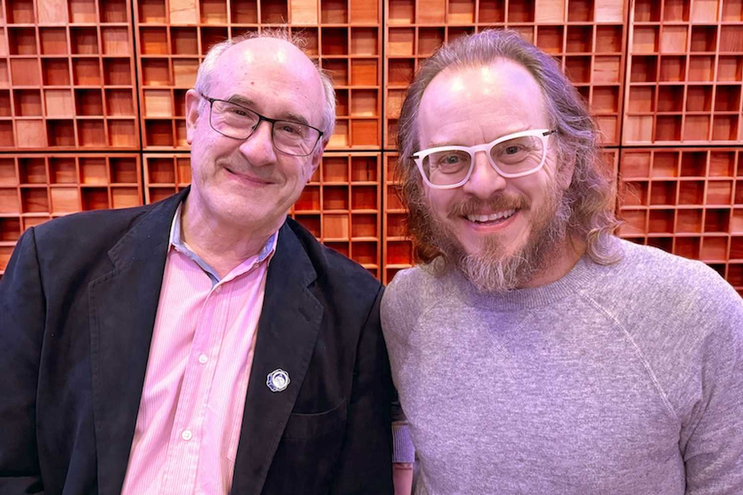 Paul Wolff, left, and Jared Vogt smiling together in front of wooden studio acoustic panels