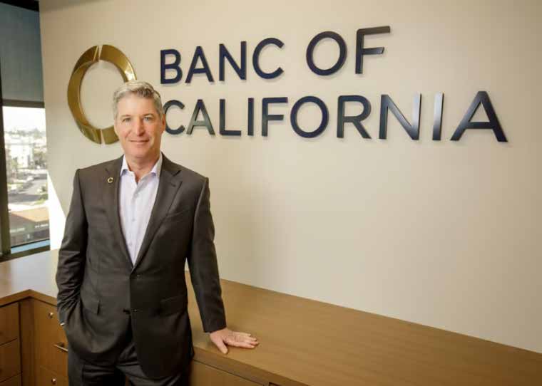 Jared Wolff standing beside the Banc of California sign in his Brentwood office
