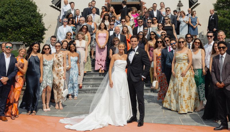 Jarrett Bauer and his bride stand with wedding guests on outdoor steps.