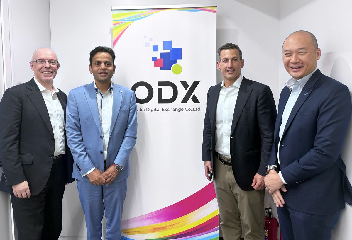Jarrod Yuster and colleagues standing beside the Osaka Digital Exchange sign in Tokyo
