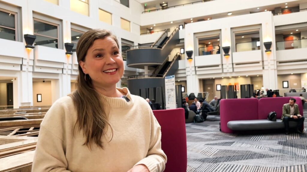 Jasmin Hume speaking during an interview in a bright conference atrium