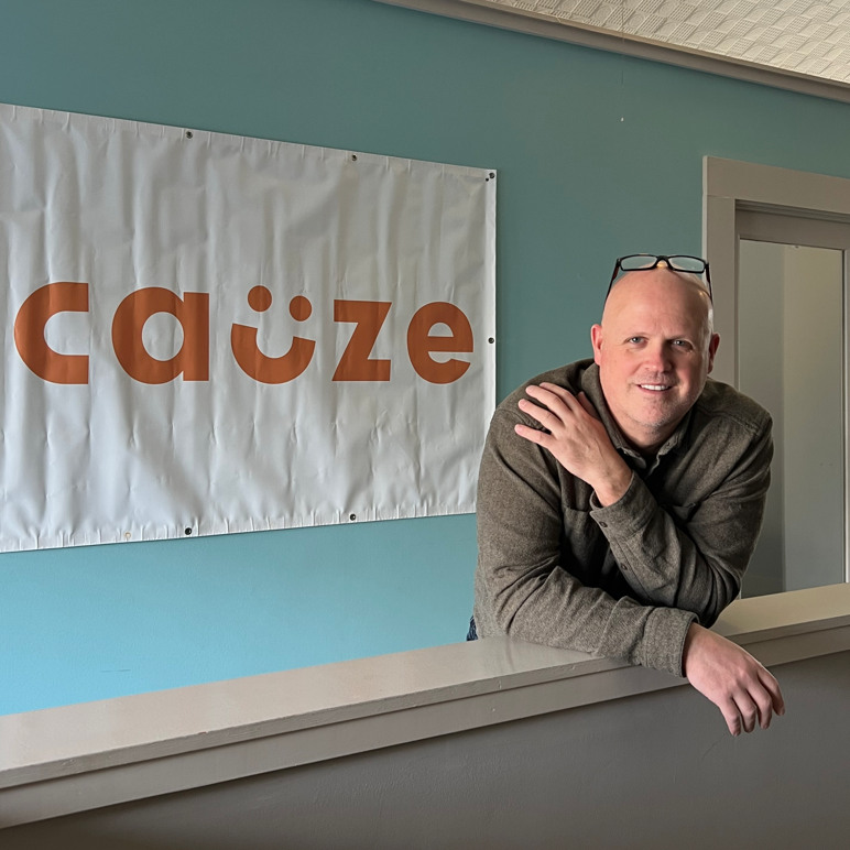 Jason Hausske leaning at a counter beside a Cauze banner