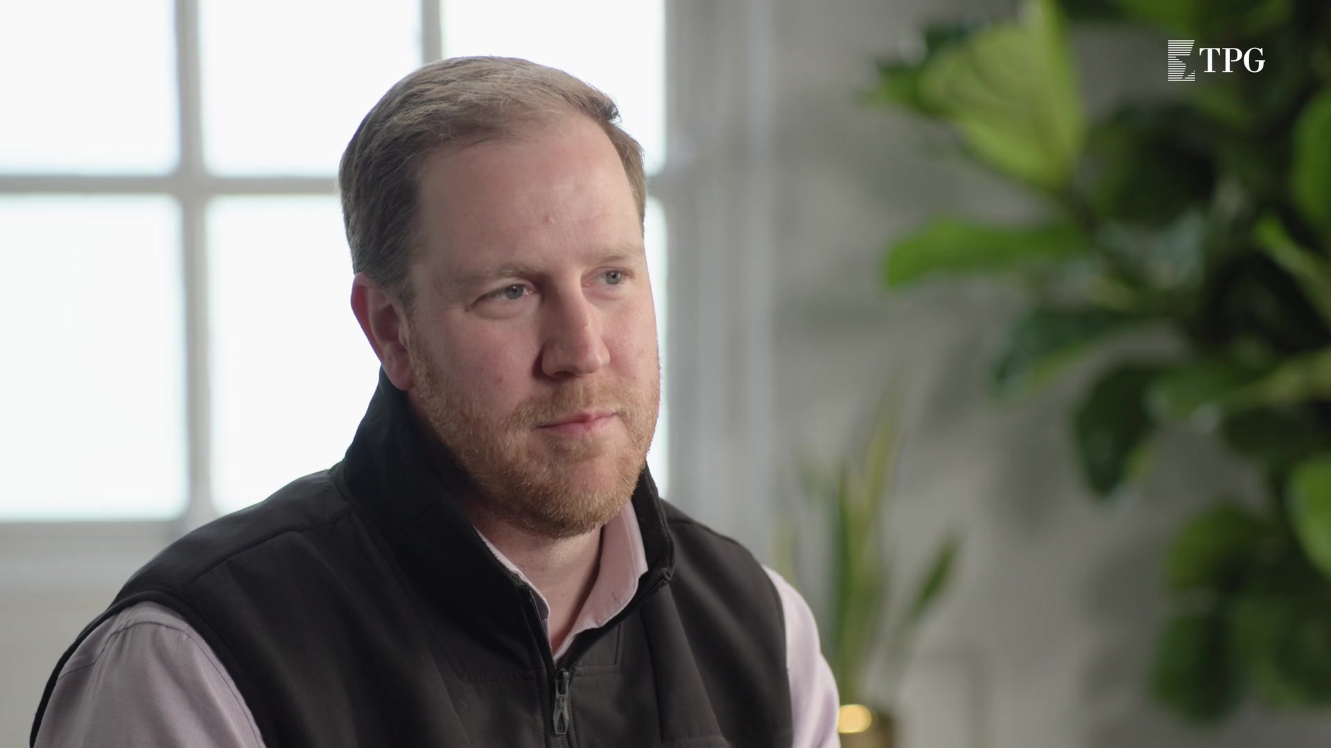 Jason Langheier seated for a filmed TPG interview, wearing a dark vest