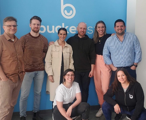 Bucketlist's customer success team gathered in front of a blue company wall