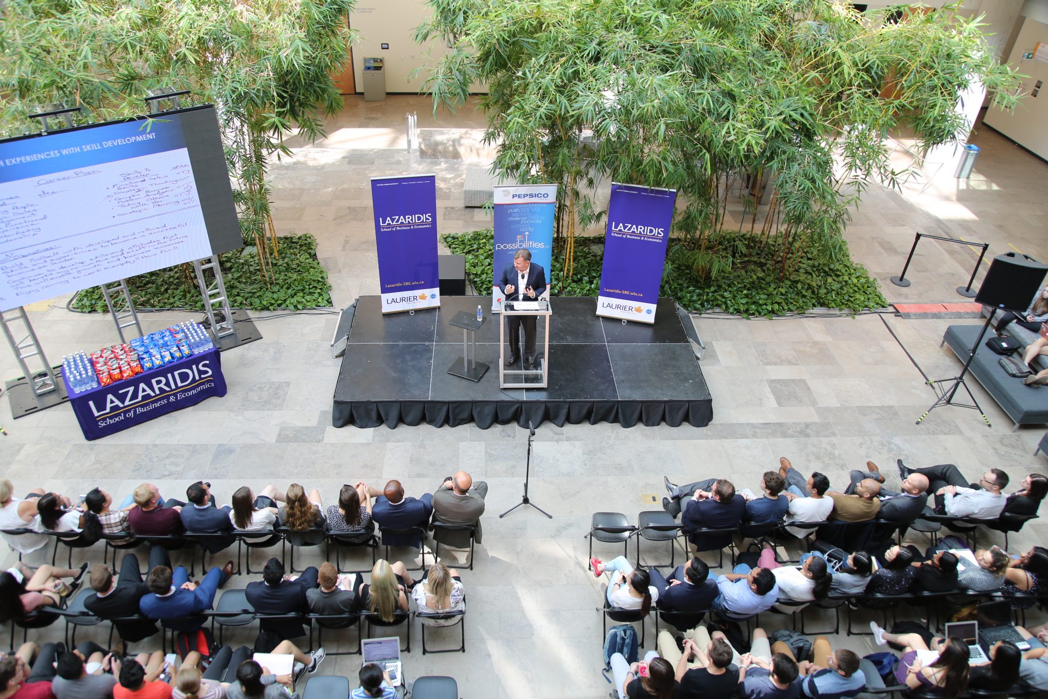 Jason McDonell speaking from a lectern to students in the Lazaridis Hall atrium