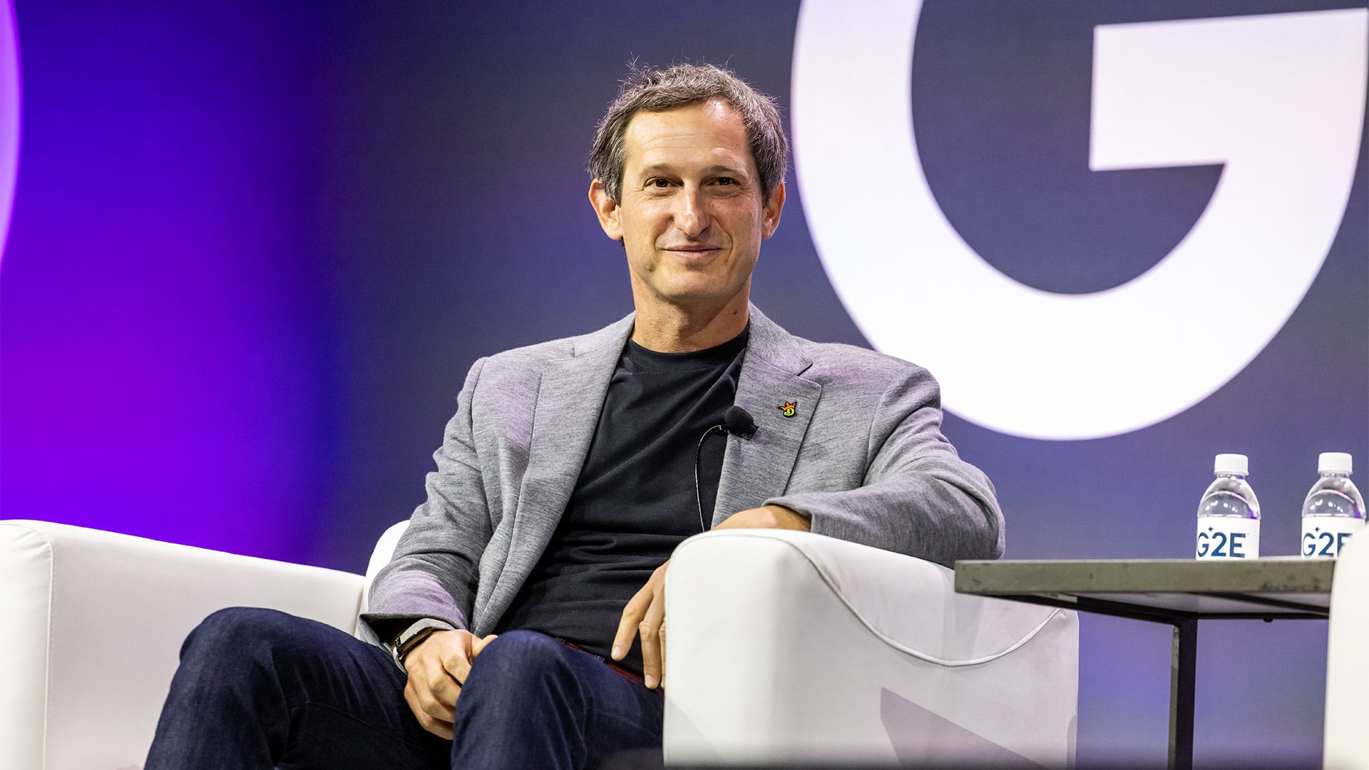 Jason Robins seated onstage at the G2E conference, wearing a gray blazer and black shirt.