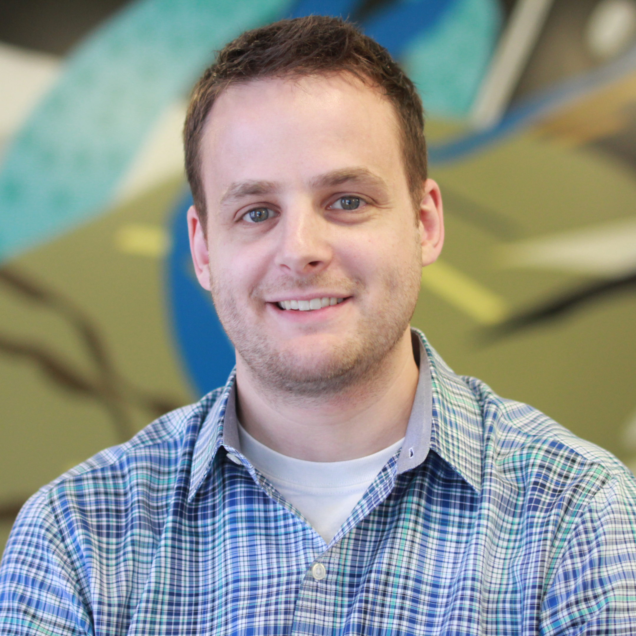 Jason VandeBoom smiling in a plaid shirt against a colorful background