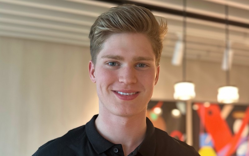 An archival photograph of Jaspar Carmichael-Jack smiling in a black polo shirt