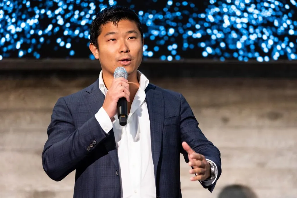 Jasper Lau speaking into a microphone and gesturing with his other hand