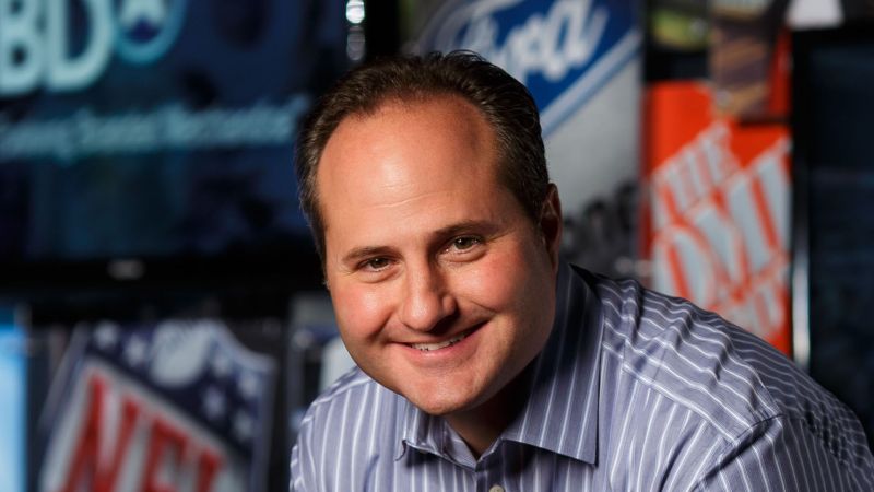 Jay Deutsch speaking at a sports merchandise event in front of sponsor logos