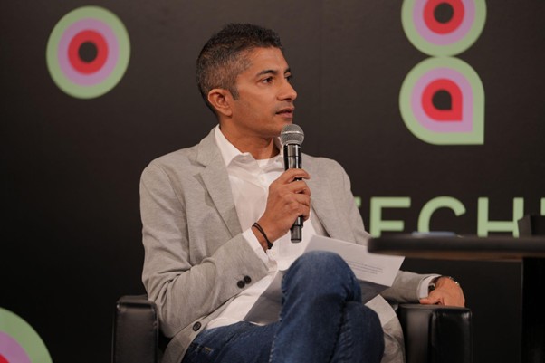 Jay Krishnan seated on stage with a microphone at TECHNIUM Global Conference