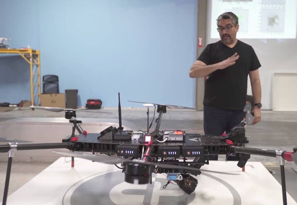 Jaz Banga gestures beside an early Airspace Interceptor drone in a workshop