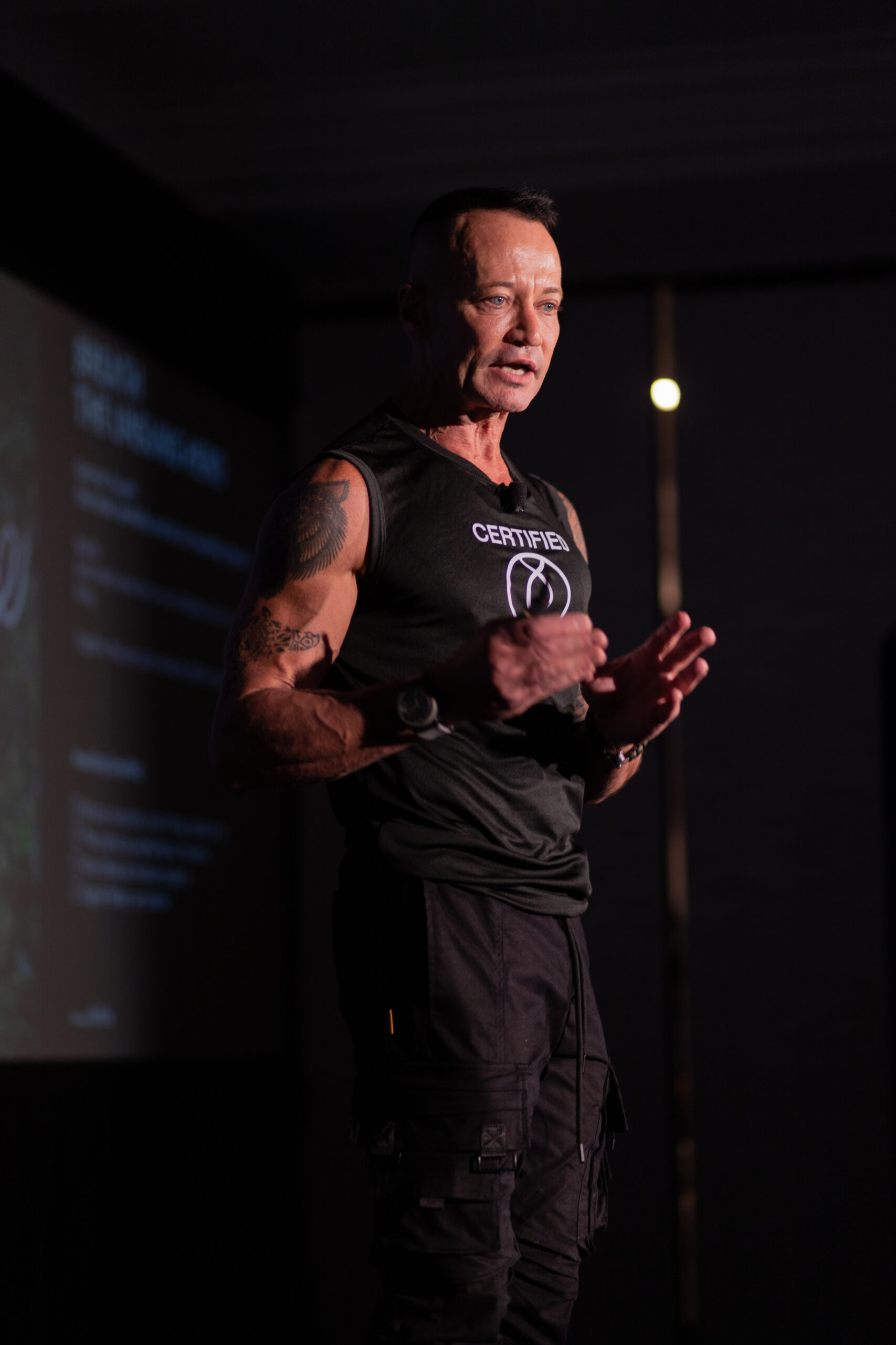 Jean Fallacara speaking, gesturing with both hands, wearing a dark sleeveless shirt