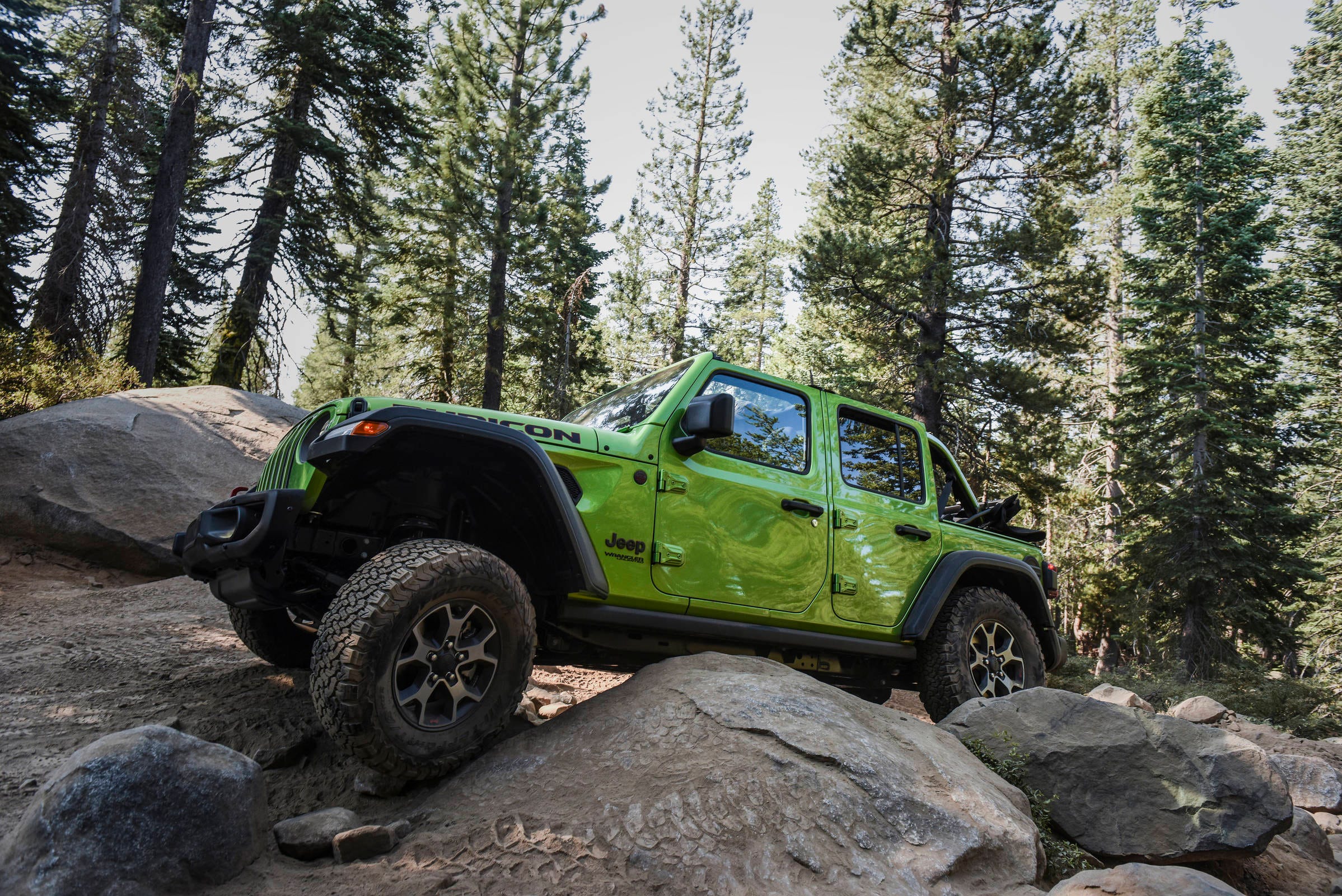 Green 2018 Jeep Wrangler Rubicon negotiating granite boulders on a wooded trail