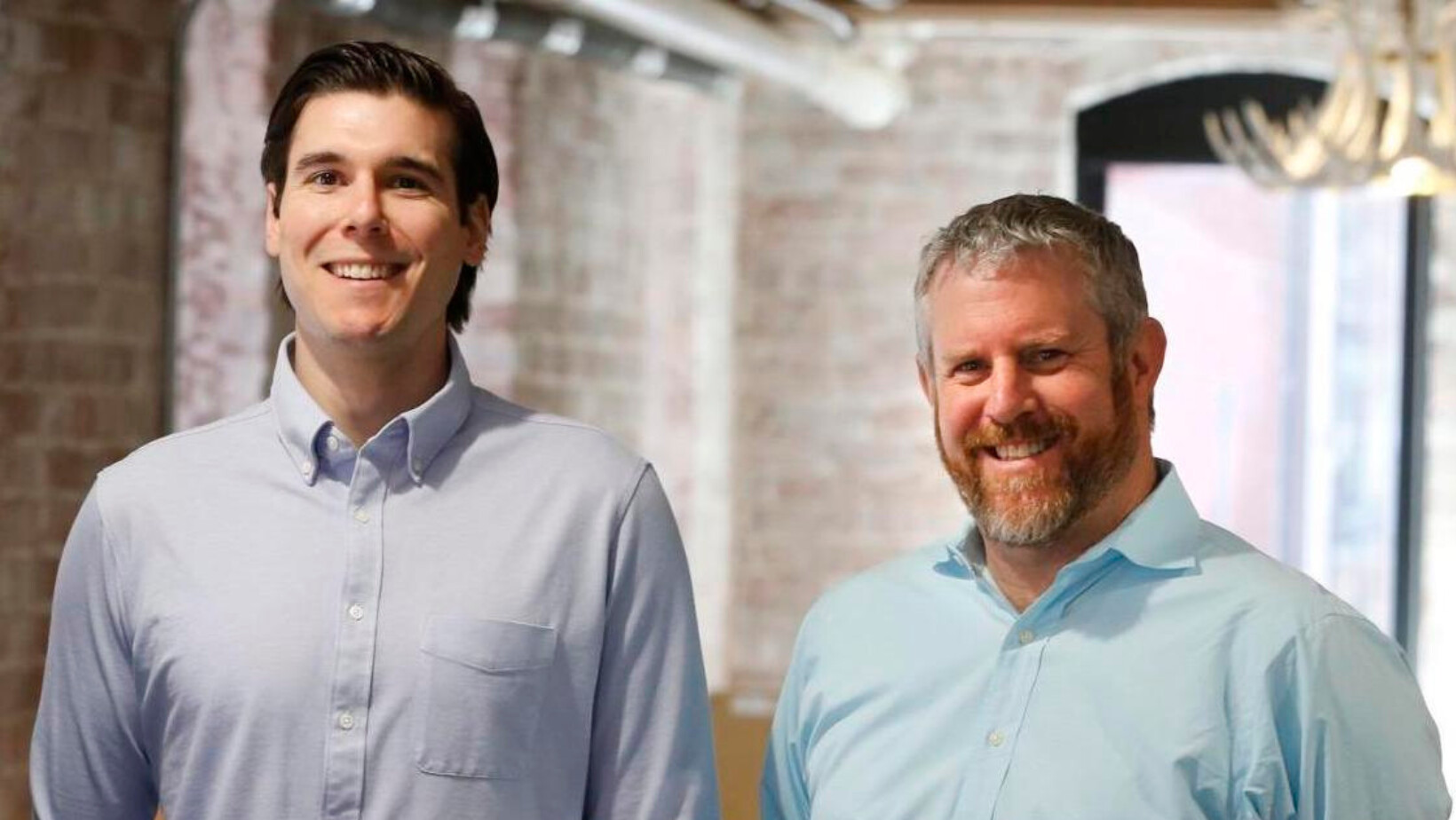 AnswersNow co-founders Jeff Beck and Adam Dreyfus standing together in a brick-walled office