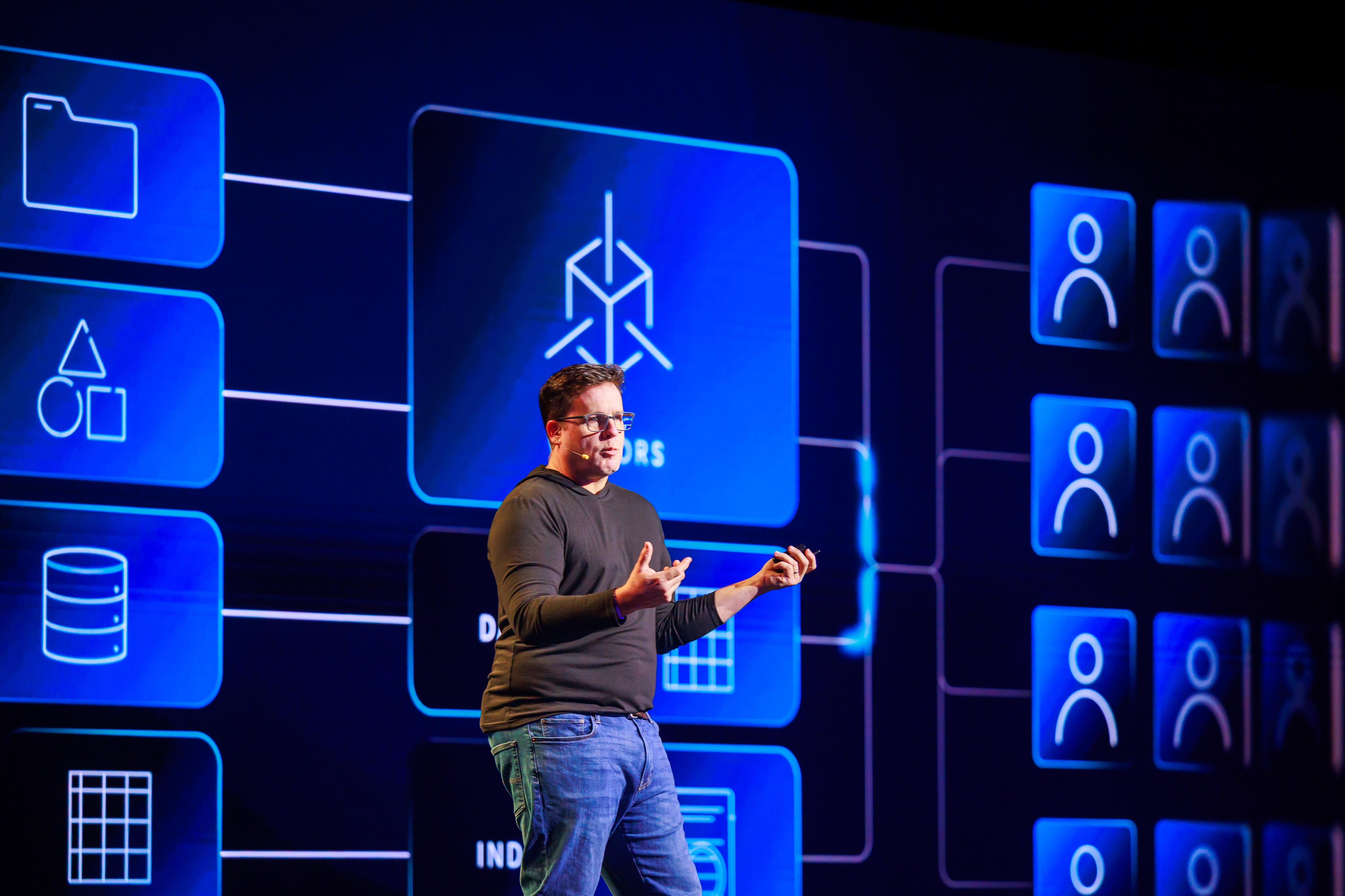 Jeff Denworth speaking onstage at VAST Forward 2026 in front of a blue systems diagram