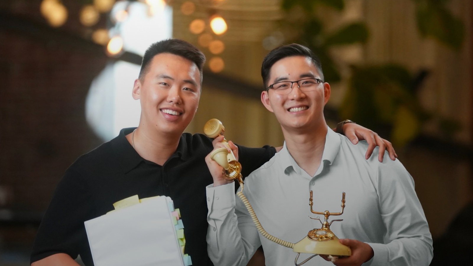 Jeff Liu, left, and Jon Wang, right, smiling together with a telephone and a binder