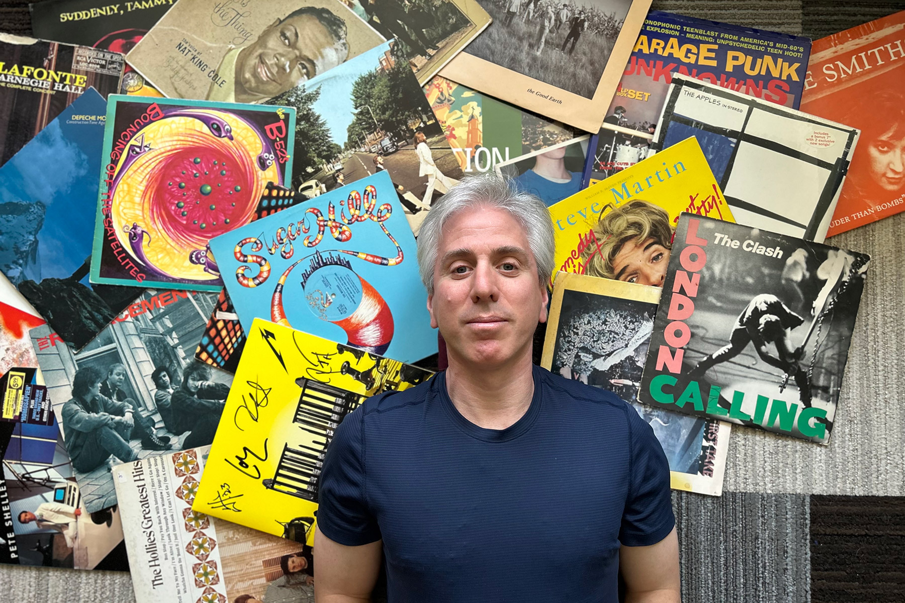 Jeff Price lying among vinyl record sleeves, including the Clash, the Apples in Stereo and Steve Martin