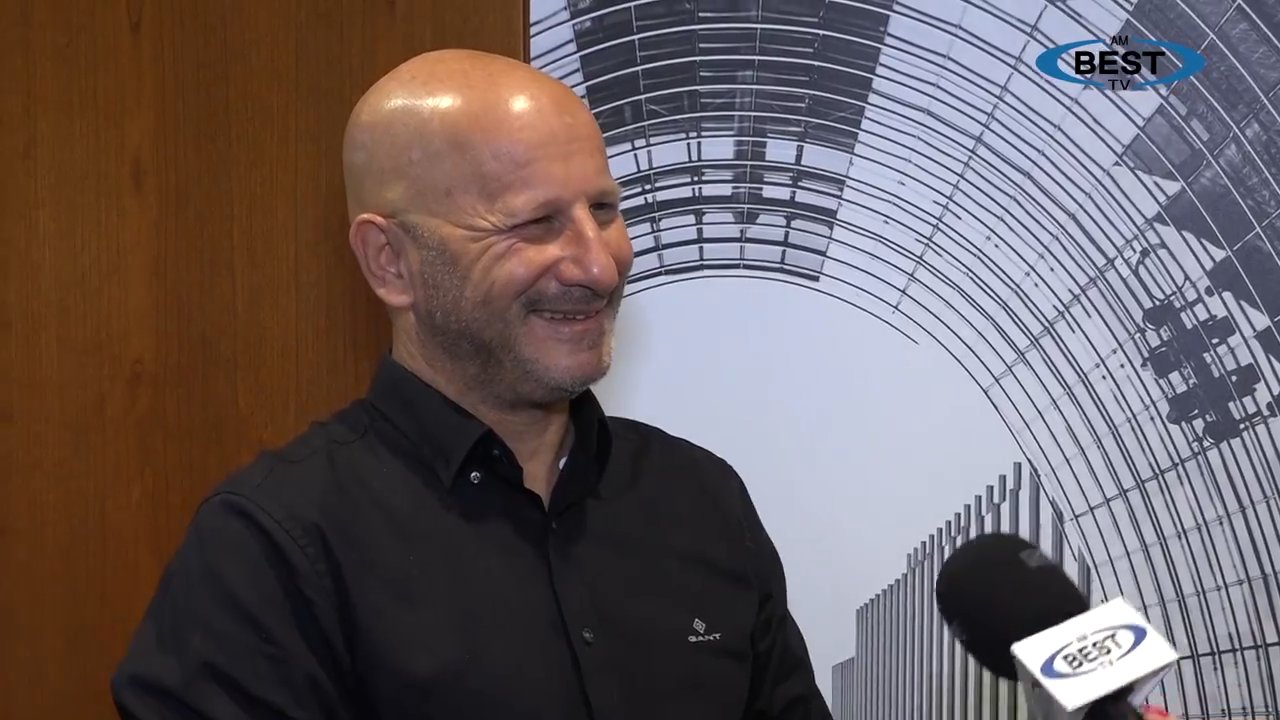 Jeff Radke smiling during an AM Best TV interview, wearing a dark shirt beside an interview microphone